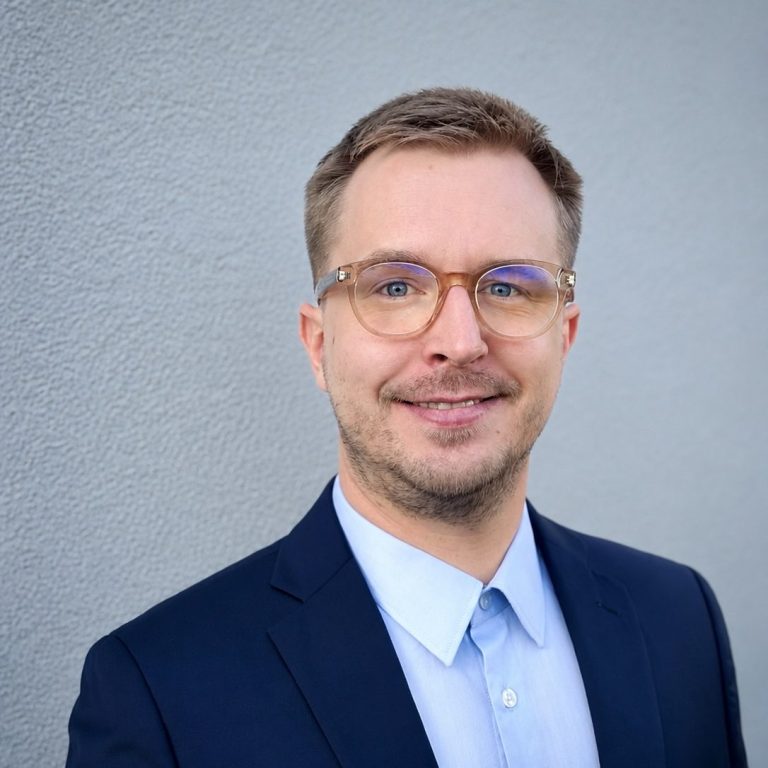 Sebastian Wolz - Bauingenieur Sympathisch lächelnder junger Mann im blauen Anzug mit Brille, Sebastian Wolz, Bauingenieur, Baubegleitung, -begutachtung
